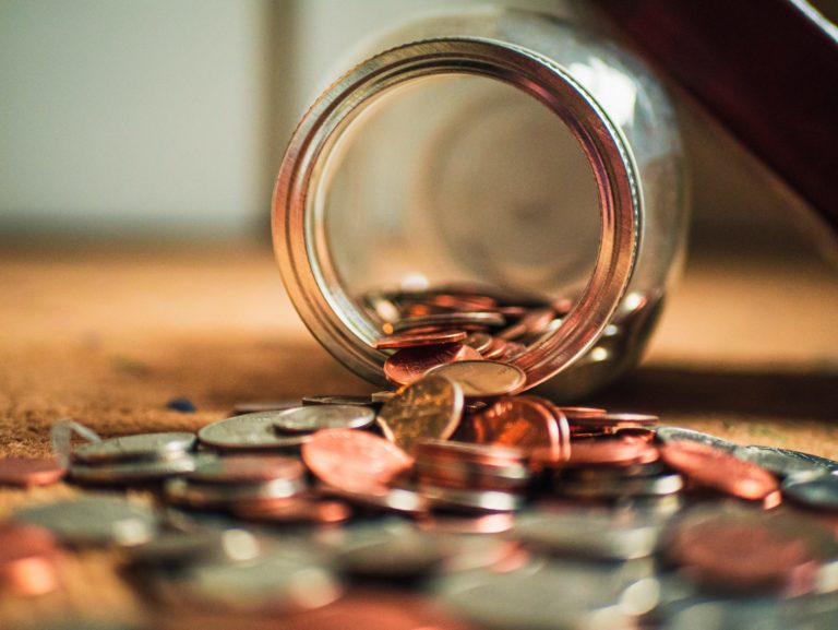 Closeup image of pennies spilling out of an overturned glass jar.
